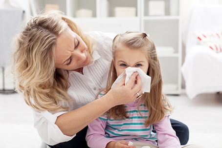 Mom helping young daughter blowing her nose